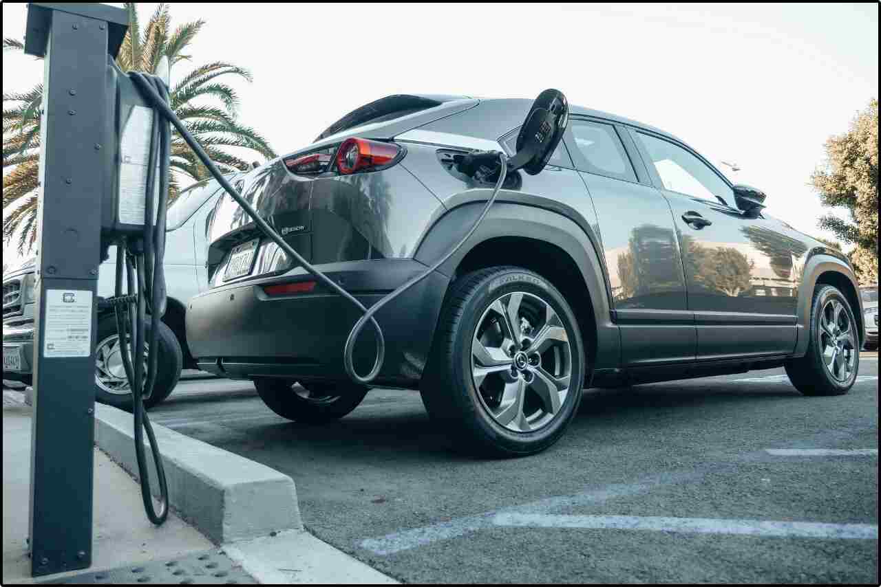 Gray electric car stationed at a charging bay, with charging cable connected.